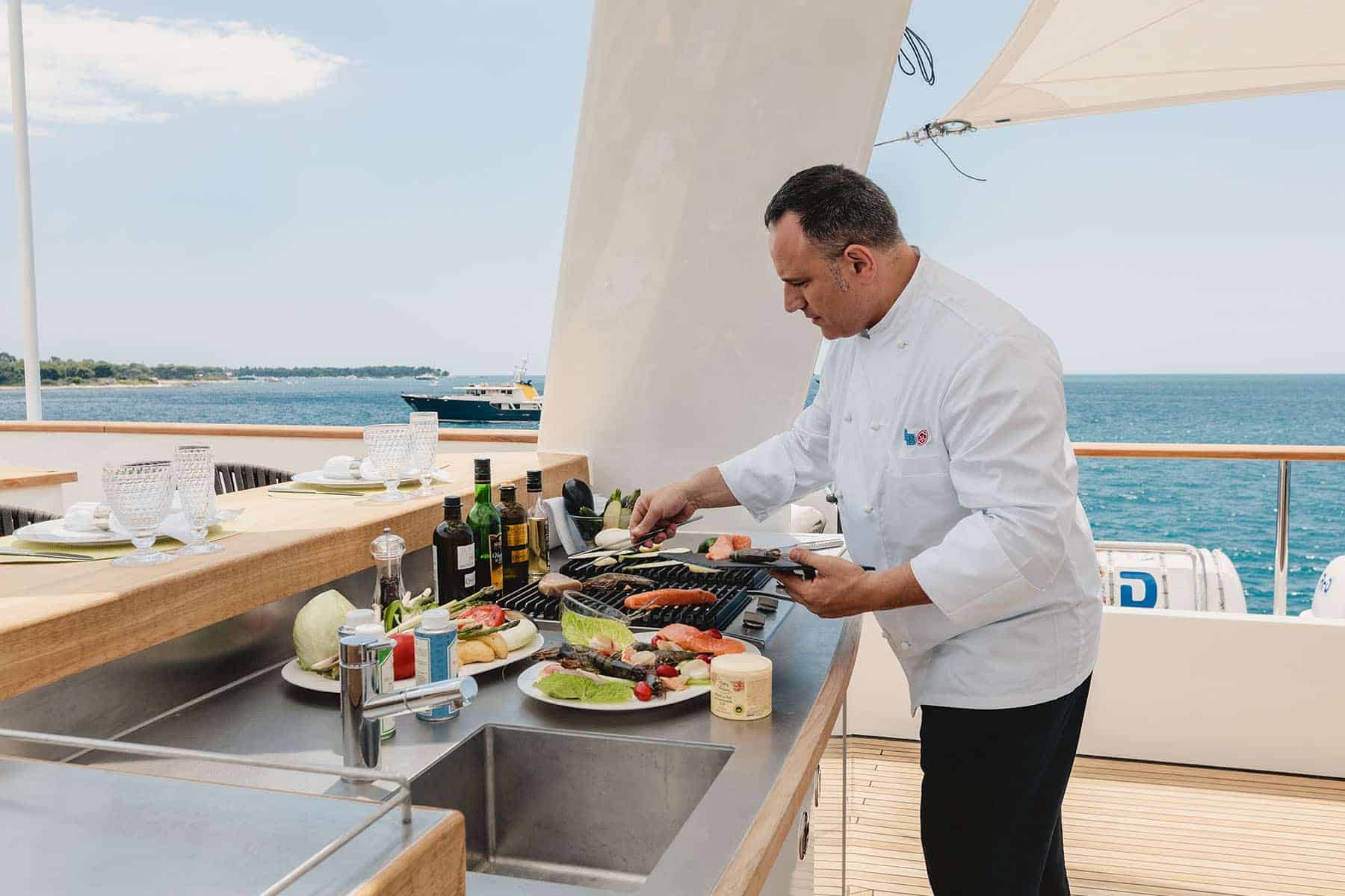 Chef grilling seafood and vegetables on a yacht deck