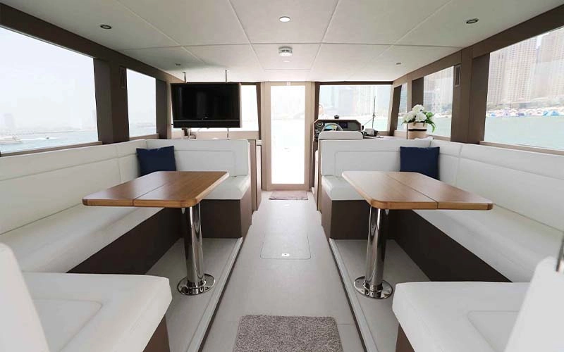 Dining area inside Cooler Bird Yacht with elegant wooden table set for eight, ambient ceiling lighting, and ocean views