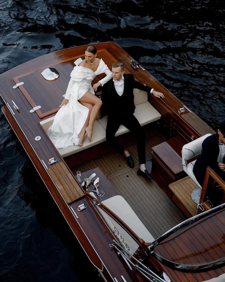 Bride and groom in elegant wedding attire relaxing on a classic wooden yacht, captured against dark ocean waters