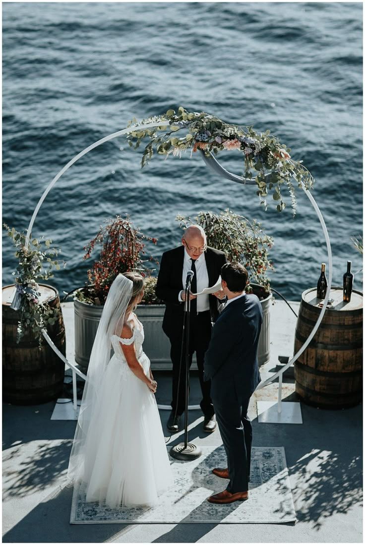 Romantic yacht wedding ceremony with bride and groom exchanging vows under a floral arch, with an officiant and ocean backdrop