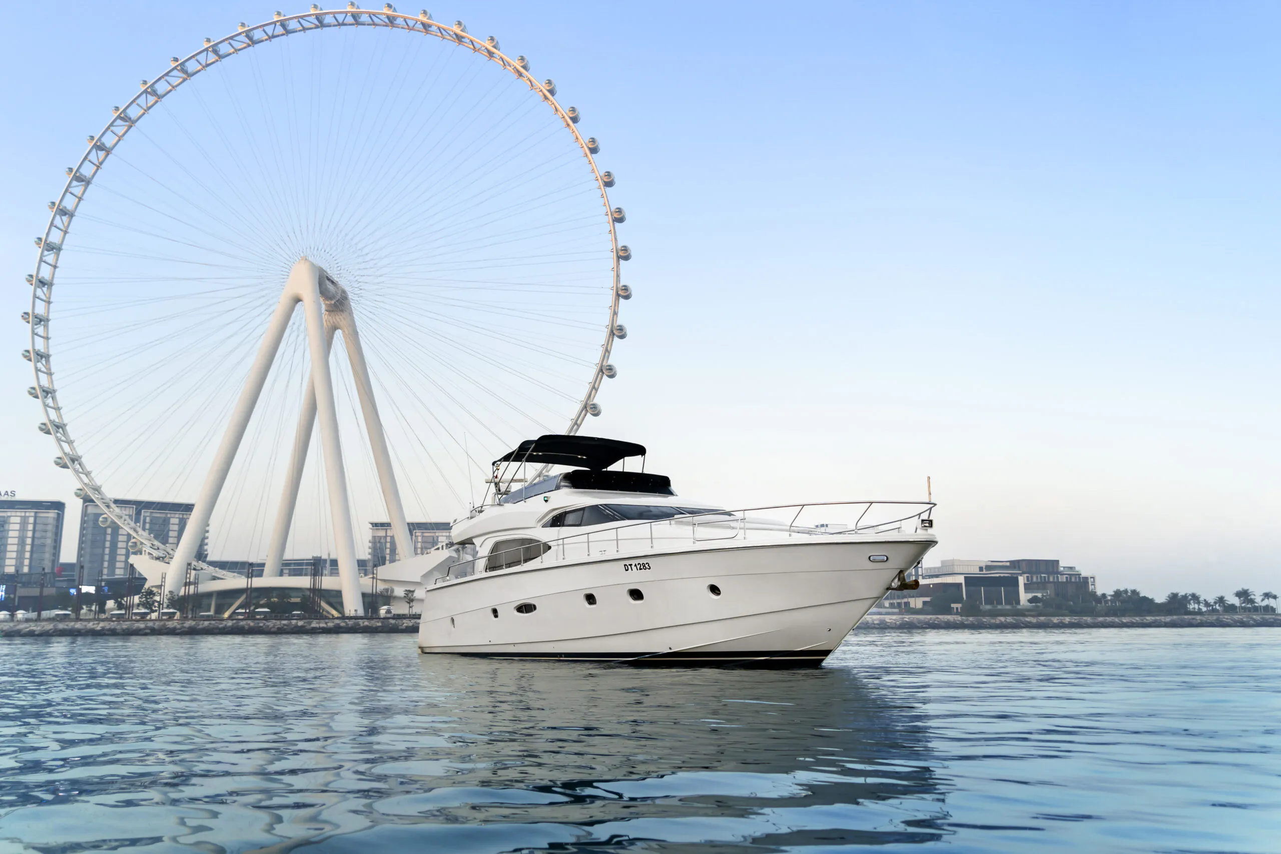 Luxury motor yacht cruising in Dubai with Ain Dubai Ferris wheel in the background on calm waters.