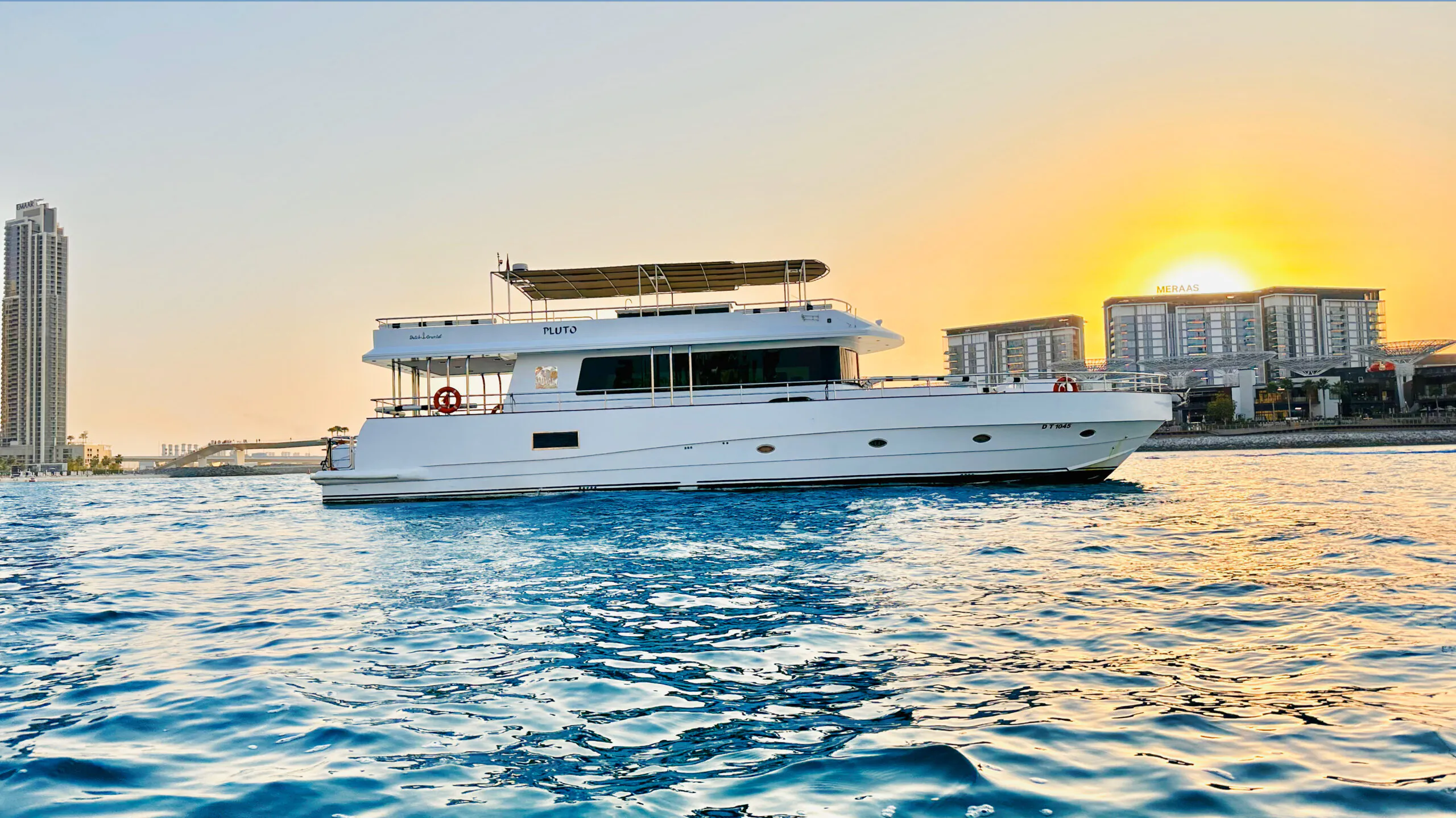 Luxury motor yacht cruising at sunset on calm blue waters with city skyline in the background