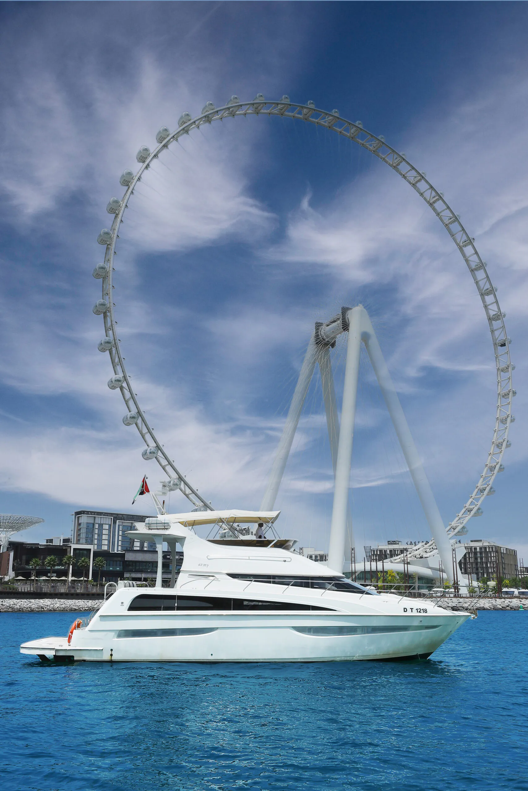 A close-up view of the Ain Dubai observation wheel against a blue sky, with part of the circular frame visible and a UAE flag flying below.