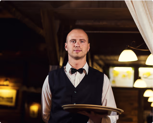 Professional waiter in formal attire holding a serving tray inside a luxury dining setting.