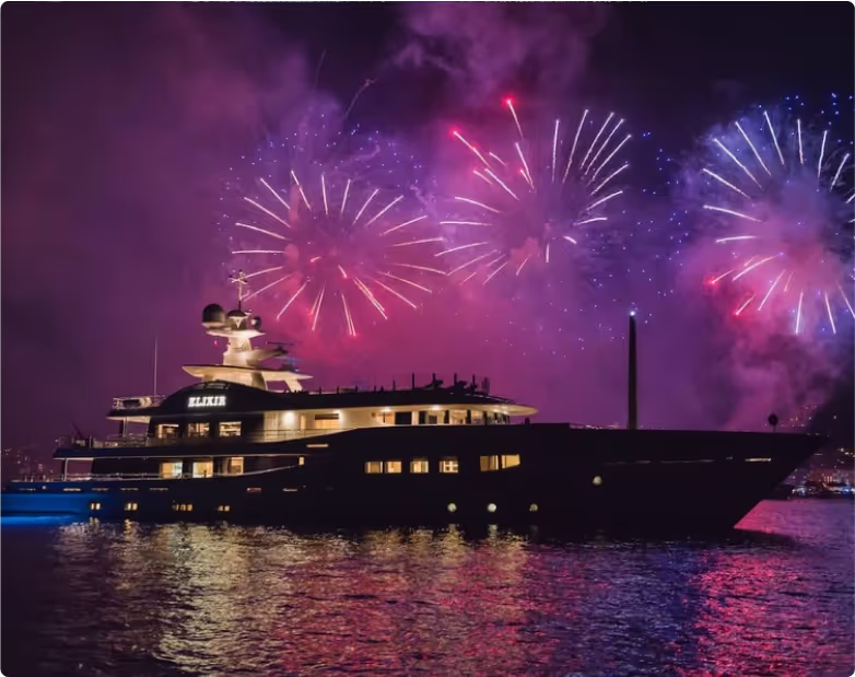Luxury yacht at night on Dubai waters with vibrant fireworks display reflecting on the sea.
