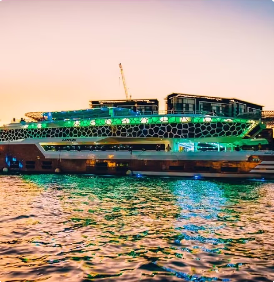 Luxury illuminated yacht cruising along Dubai waterfront at sunset with modern skyline in the background.